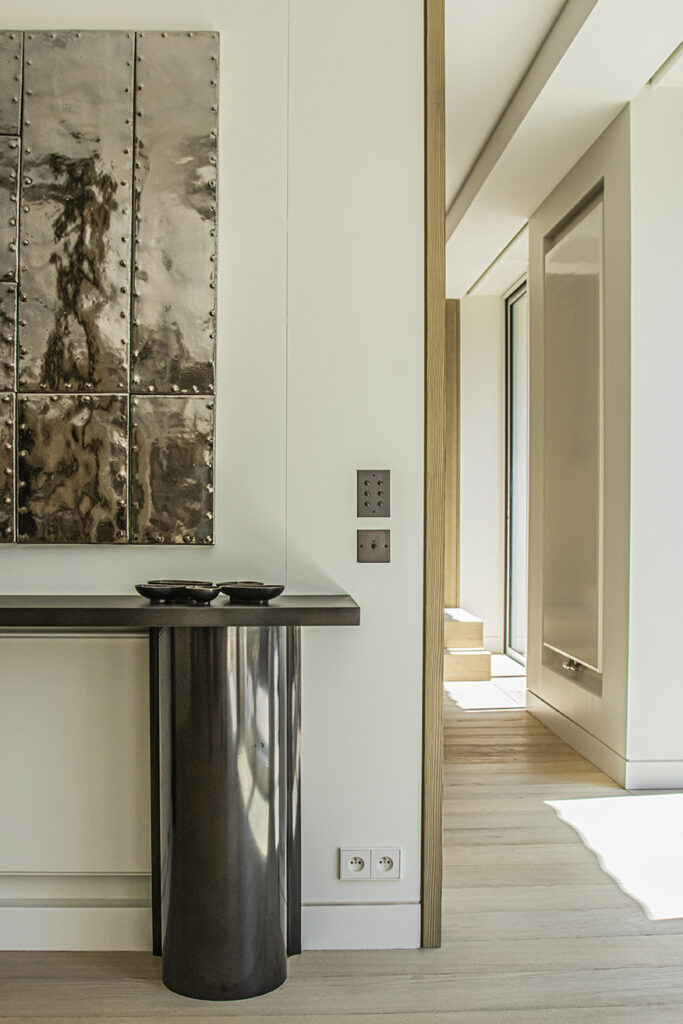 Custom interior detail featuring a sculptural console table, metal wall artwork and bespoke finishes in Neuilly near Paris.